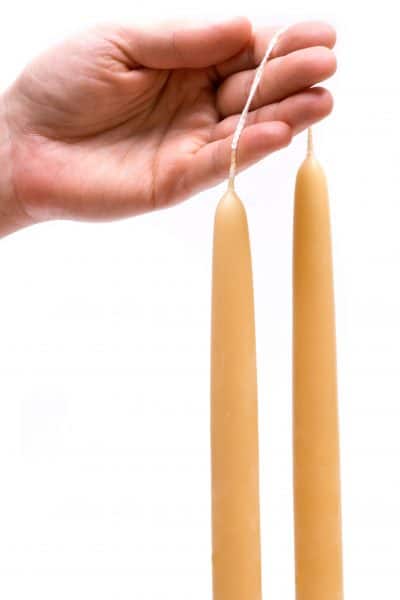 A hand holding two beeswax taper candles