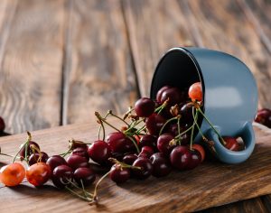 A blue cup of fresh cherries spilled over