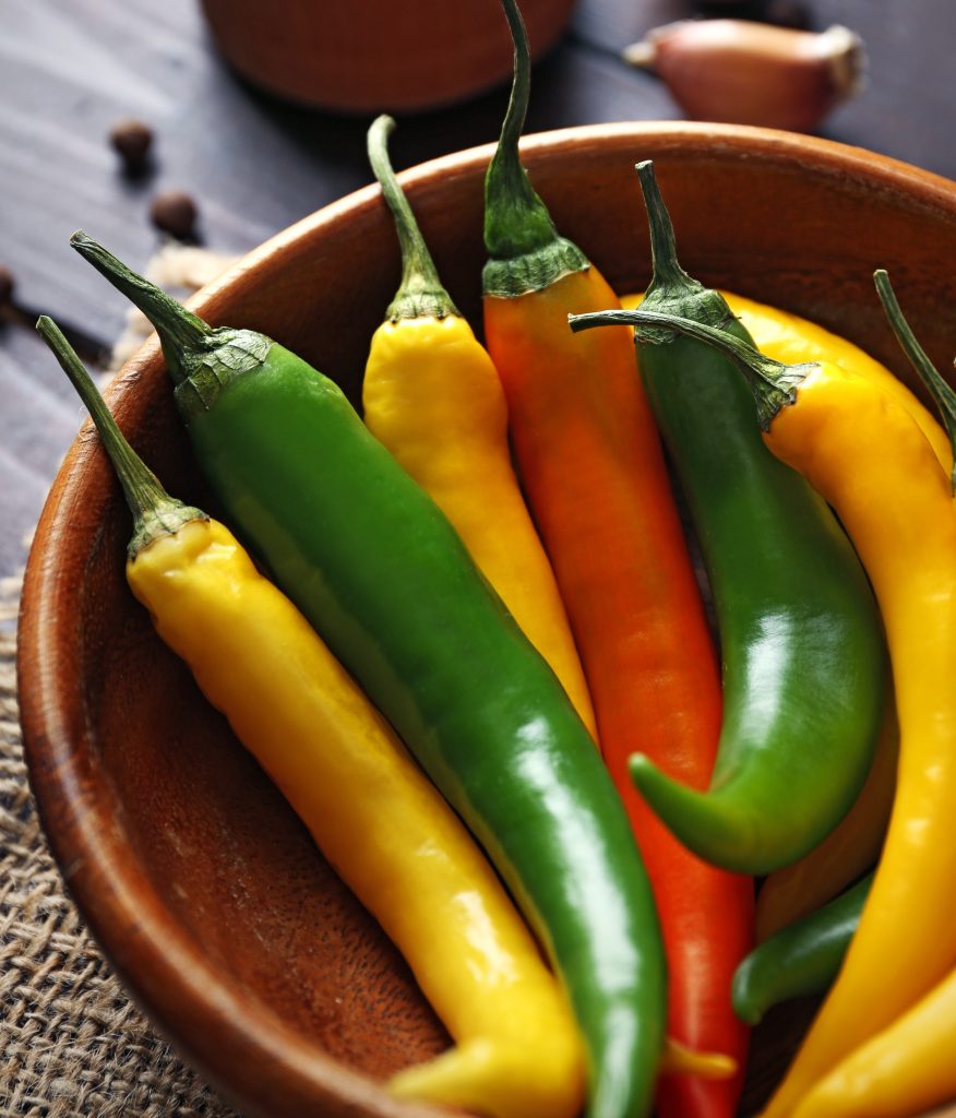 A wooden bowl with orange, yellow and green hot peppers
