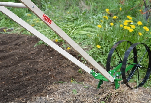 The wheel hoe prepares the rows for planting easily. In a deep mulch system, the mulch is raked aside, exposing the soil, before the wheel hoe passes down the garden bed. In early spring, much of the mulch that was laid down the previous fall is already decomposing, so there is only a light mulch to move aside. I used the cultivator teeth on the double wheel hoe to move the dirt and get the bed ready for planting. Any weeds that had managed to germinate under the thin mulch were nipped off with the cultivator teeth. Then I switched to the right and left plow blades to create a shallow furrow