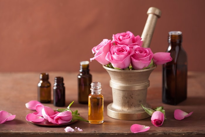 Pink roses in a mortar and pestle. Rose petals scattered around and apothecary bottles on a table