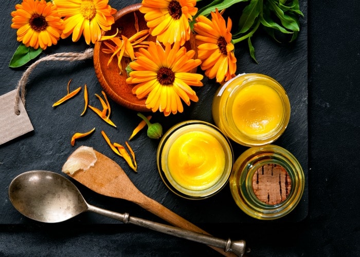 Fresh calendula flowers by glass jars full of yellow salve