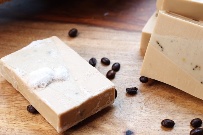 a bar of coffee espresso soap, covered in suds, surrounded with scattered coffee beans