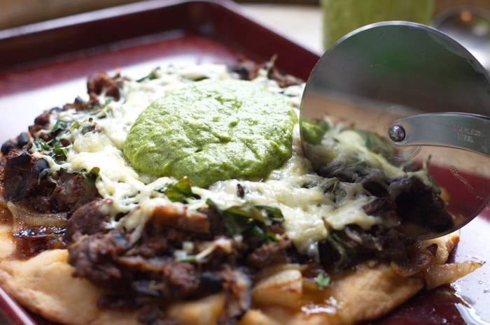 Cutting asparagus pesto pizza with a pizza cutter