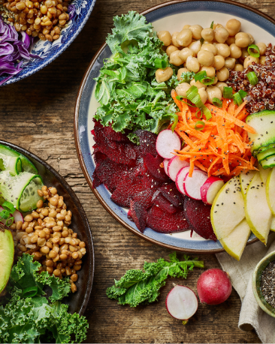 a collection of 3 healthy bowls with chickpeas, avocado, shredded carrots and red cabbage, kale, and other vegetables visible on the surface of the rice bowl.